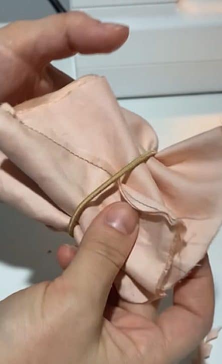 close up of hands holding red silk scrunchie and tan elastic band